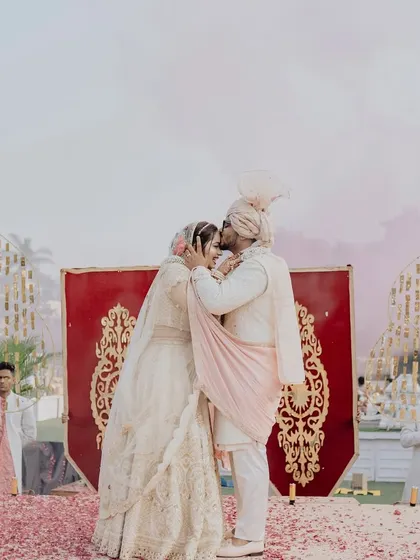 A sweet kiss shared on the varmala stage, surrounded by a carpet of red rose petals. These are the romantic moments that make all the planning worthwhile.