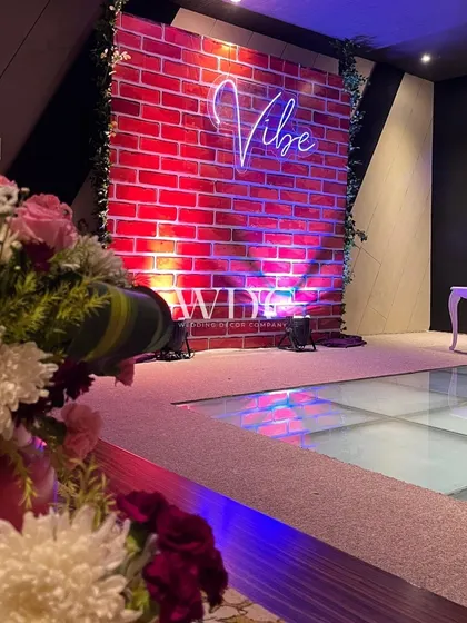 A perfect photo spot. A 'Vibe' neon sign against a brick wall, with a glass-floored dance area in front, sets the stage for a night of fun and dancing.