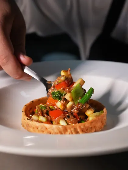 A spoonful of the flavourful tadka-tossed vegetables being placed into the tart shell. Every component is carefully assembled to create the perfect bite.