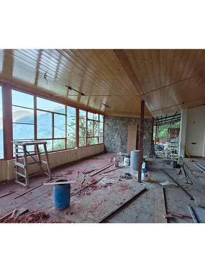 The interior of the homestay extension nearing completion. The warm wood-paneled ceiling and large windows create a cozy and inviting atmosphere, perfect for enjoying the mountain views.