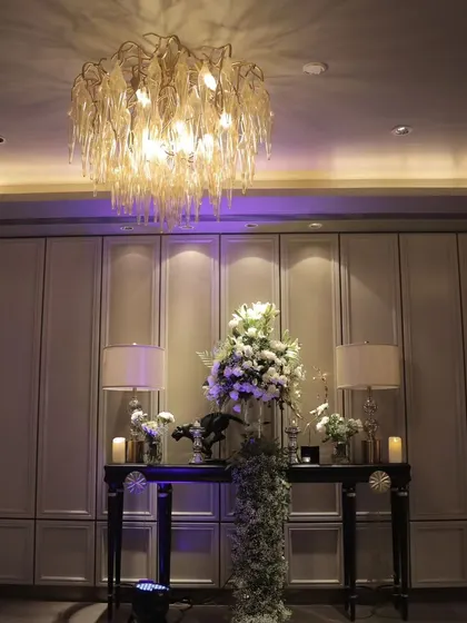 An elegant console table setup in a lounge area, featuring a large floral arrangement, classic table lamps, and a statement chandelier overhead. This shows our attention to detail in styling every corner of an event space.