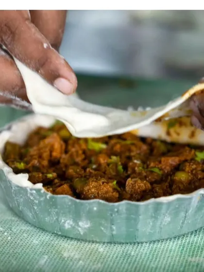 Carefully placing the pastry lid over the spicy Kolhapuri chicken filling. This fusion dish has become a huge hit with my customers.