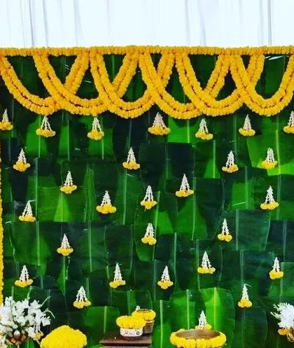 A close-up of a backdrop made from banana leaves, decorated with garlands of marigold and white jasmine flowers.