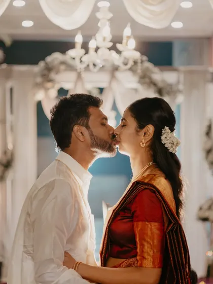 The couple shares a kiss under a grand chandelier, a romantic highlight from their South Indian wedding.