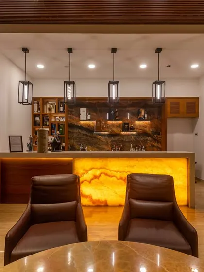 A sophisticated home bar with an onyx-lit counter that creates a warm, ambient glow. The setup includes a marble backdrop, custom shelving for glassware, and comfortable leather seating.