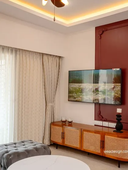The TV unit in this neo-classical home features a rich maroon accent wall with ornate mouldings and a cane-fronted console, blending traditional details with modern needs.