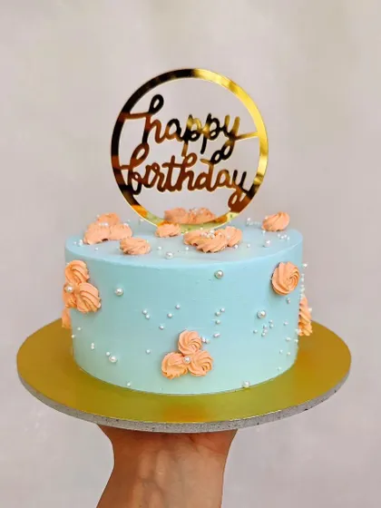 A lovely pastel blue cake with peach-colored buttercream rosettes and a gold acrylic topper.