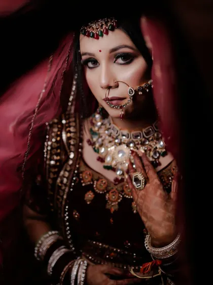 A striking bridal portrait with a red-lit background. The bride's direct gaze and the dramatic lighting create a powerful and confident image.