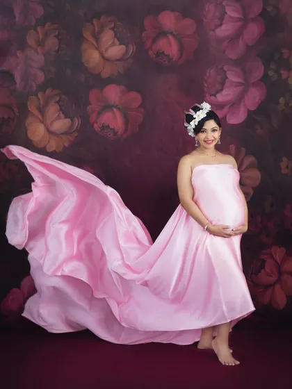 A touch of whimsy and romance with this flowing pink satin gown against a floral backdrop. The flower crown adds a delicate, feminine touch to this beautiful studio portrait.