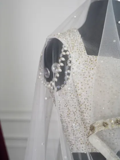 A close-up detail of the pearl and sequin work on the shoulder of the ivory lehenga. This shot reveals the delicate, leaf-like patterns and the sheer craftsmanship involved in the embellishment.