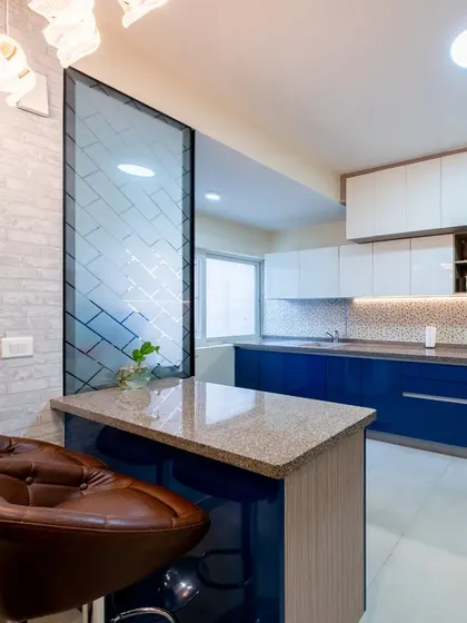 A modern kitchen with a breakfast bar and stylish leather stools. The design features a striking blue and white color scheme and a frosted glass partition.