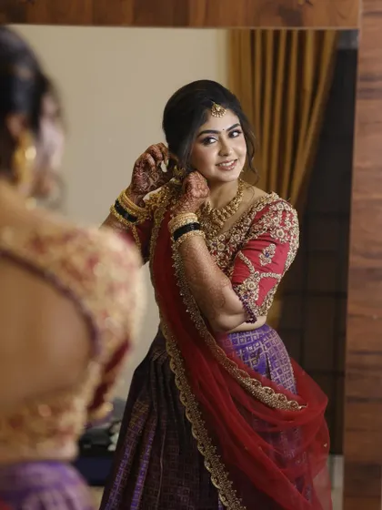 A classic "getting ready" shot. Nithya looks in the mirror, admiring her reception look, which features a traditional half-saree and glamorous makeup.