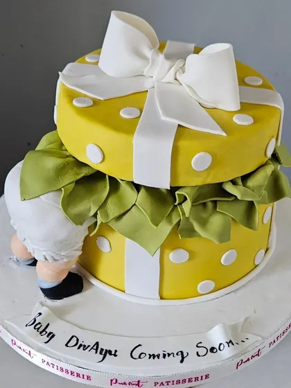 Another view of the gift box baby shower cake, showing the "Baby Divayu Coming Soon" message on the edible banner.