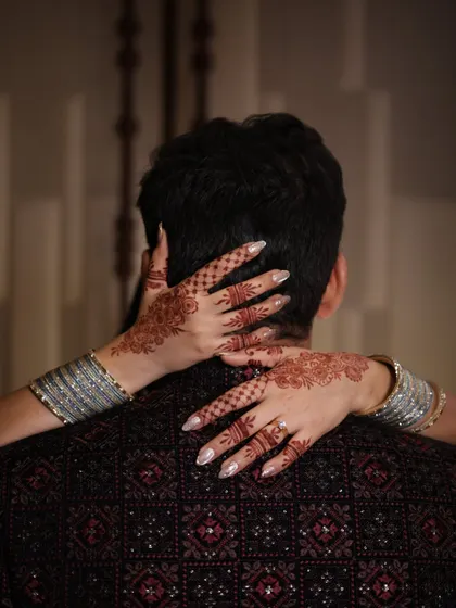 An intimate shot focusing on the bride's henna-adorned hands wrapped around the groom's neck.