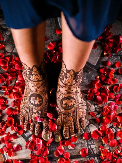 A top-down view of the beautiful bridal feet mehendi, showcasing the intricate details and the scattering of red rose petals.