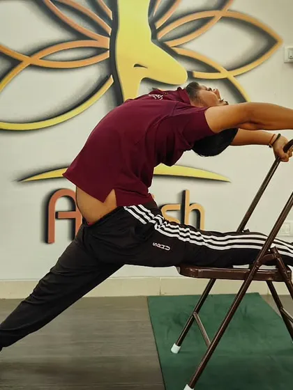 An advanced student uses a chair to deepen a split and backbend simultaneously, showcasing incredible flexibility.