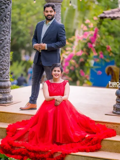 A powerful and elegant pose on the steps. The bride-to-be is seated, her vibrant red gown flowing down, while her partner stands behind her, creating a classic and cinematic couple portrait.
