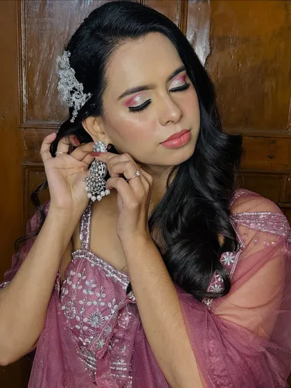 The client adjusting her earring, a candid moment that shows off the makeup and hairstyle.