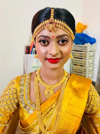 A classic muhurtham look for my bride. The focus here is on traditional elements: a neat hair bun, a bright red bindi, and gold jewellery, all tied together with makeup that enhances her features beautifully.