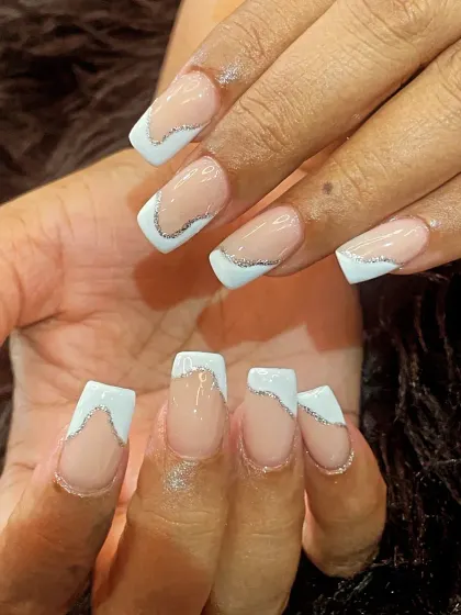A creative twist on the French manicure. This design features an abstract, wavy silver glitter line separating the natural base from the soft white tip on square nails.