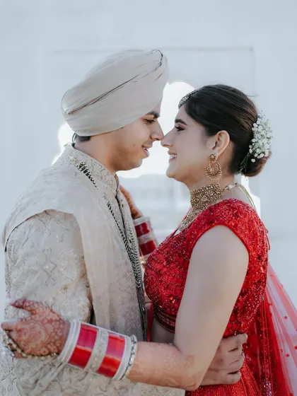 A close-up portrait of a couple in their wedding attire. The groom's turban and the bride's red lehenga create a classic and vibrant image of love.
