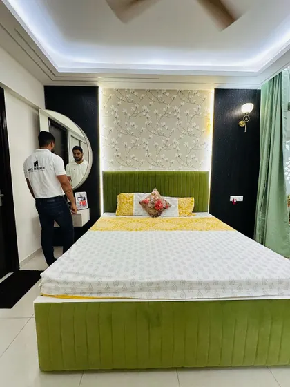 This guest bedroom features a vibrant green upholstered bed and a feature wall with floral wallpaper and dark paneling. A small, floating dressing table with a round mirror completes the look.