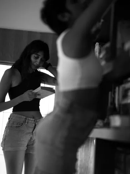 A candid black and white photo of two women in a room with bookshelves. One is reading while the other looks on, creating a natural, story-driven scene of everyday life.