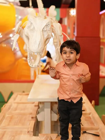 A young boy stands next to a giant T-Rex skeleton, part of our dinosaur-themed decor.