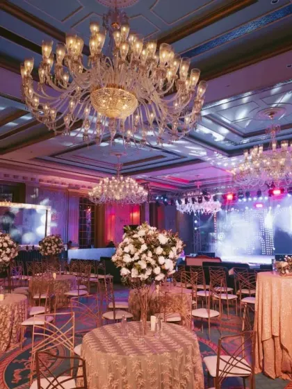 The sangeet ballroom with elegant table settings, grand chandeliers, and a full-scale concert stage, ready for a night of celebration.
