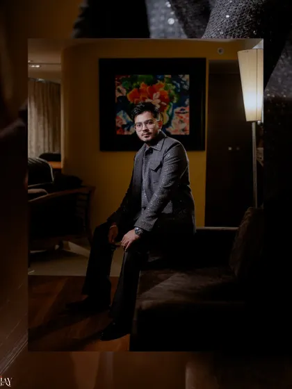 A stylish portrait of the groom seated in a dimly lit room, exuding confidence.