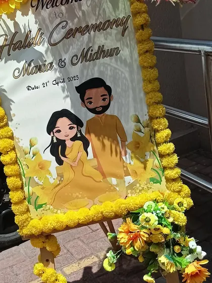 A personalized welcome easel for a Haldi ceremony, featuring a cute caricature of the couple and decorated with marigold flowers.