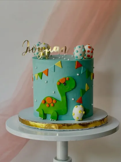 This dinosaur-themed cake is perfect for a dino lover. It features a green brontosaurus, dinosaur eggs, and a festive bunting on a teal buttercream cake.