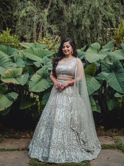 A beautiful portrait of Ashwini in her reception lehenga, set against a backdrop of large green leaves.