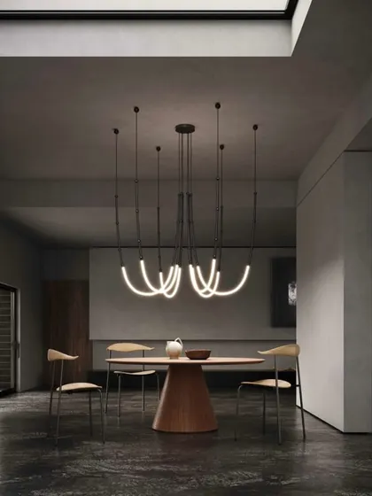 The Leda system configured as a chandelier over a dining table. The curved, glowing forms create a soft, organic contrast to the sharp lines of the modern furniture.