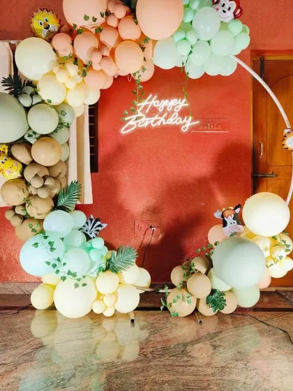 A close-up of the pastel jungle animal theme, featuring a 'Happy Birthday' neon sign and cute animal cutouts peeking through the balloons.