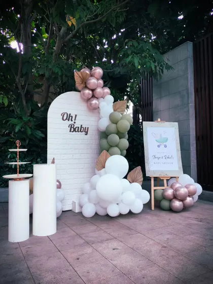A simple and chic outdoor baby shower setup. The white brick-textured backdrop with the "Oh Baby" sign and an elegant balloon garland is perfect for a minimalist celebration.