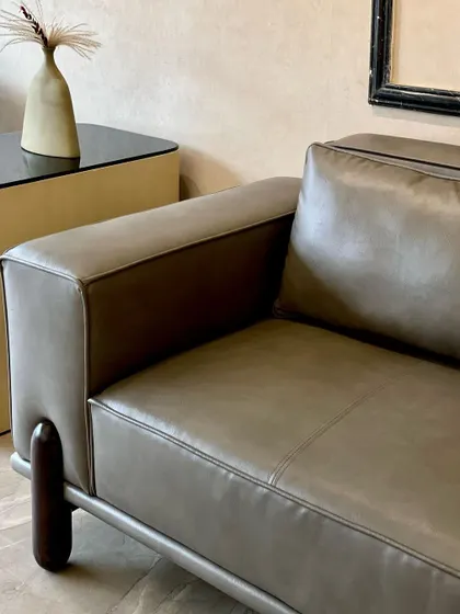 Another angle of the 'Academia Sofa', highlighting its sleek profile and the beautiful contrast between the grey leatherette and the warm wooden legs.