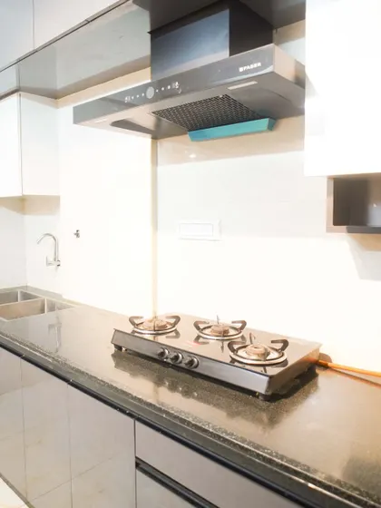 This image showcases the functionality of a modern kitchen with a three-burner gas stove on a granite countertop. The sleek, handleless design of the beige cabinets contributes to the kitchen's clean and uncluttered appearance.