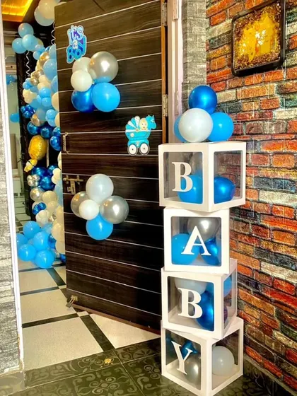 "BABY" blocks used as a decorative element for a baby-related event. The transparent boxes are filled with blue, white, and silver balloons, matching the rest of the party's decor.