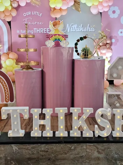 A full view of a fairy-themed third birthday, showcasing marquee letters spelling out the name 'Nithiksha', multiple cake plinths, and a large light-up number '3'.