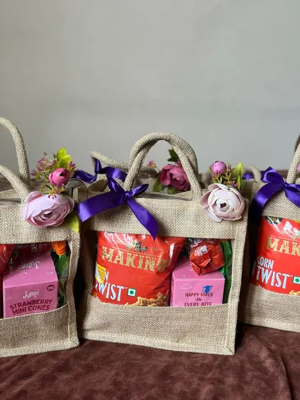 Jute bags with a clear window, filled with snacks and decorated with purple ribbons and flowers.