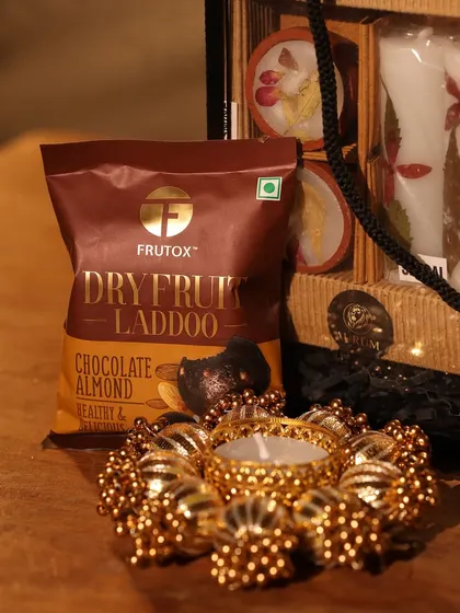 A close-up of the healthy dry fruit laddoos and the ornate golden diya from the hamper.