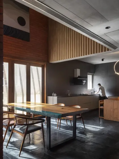 The kitchen and dining area in the Brick House, where a double-height ceiling and large doors create an airy, light-filled space. The material palette of brick, wood, and dark stone is honest and tactile.