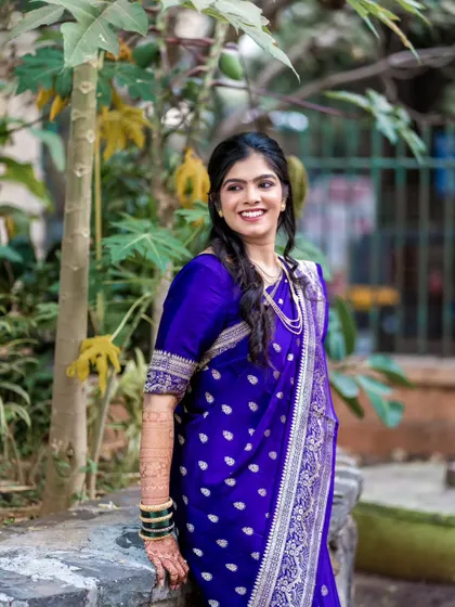 A bride enjoying a quiet moment outdoors. The natural greenery provides a beautiful contrast to her vibrant blue saree.