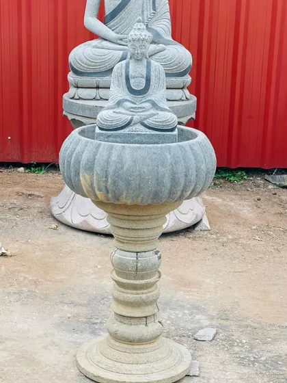 A stone Buddha statue placed inside a lotus-shaped water fountain bowl. This combines two classic garden elements into one feature.