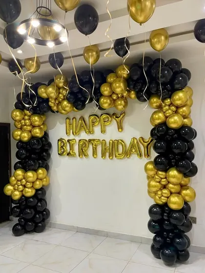 A classic black and gold birthday decoration. This setup includes a large organic balloon arch and 'Happy Birthday' foil letters, creating a timeless and celebratory look suitable for any age.