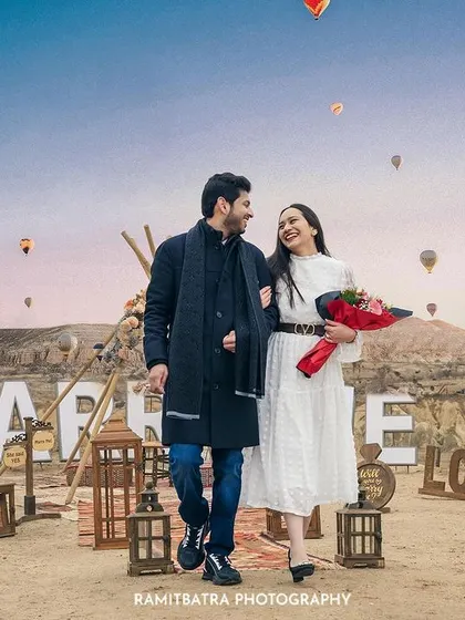 The newly engaged couple walks arm-in-arm after a surprise proposal in Cappadocia, with a bouquet of red roses.
