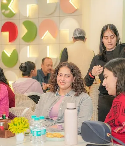 Parents relaxing at a table, chatting and enjoying refreshments while the kids play.