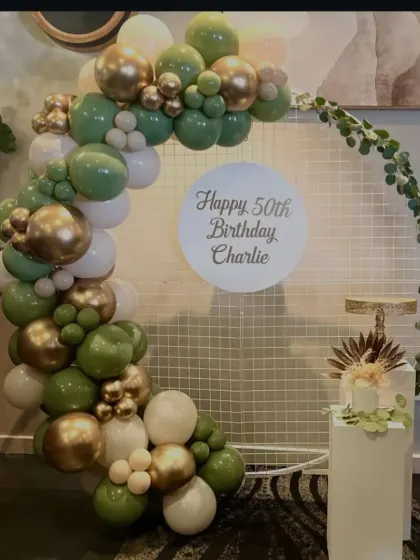 An elegant and earthy theme for a 50th birthday. This design uses a mesh ring backdrop with an organic balloon arch in shades of green, white, and gold for a sophisticated look.