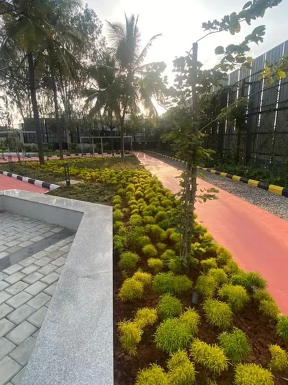 A vibrant red jogging path at Vaishnavi Tech Square is lined with neatly arranged shrubs and young trees. This demonstrates our approach to combining functional elements for fitness with organized, aesthetic planting.